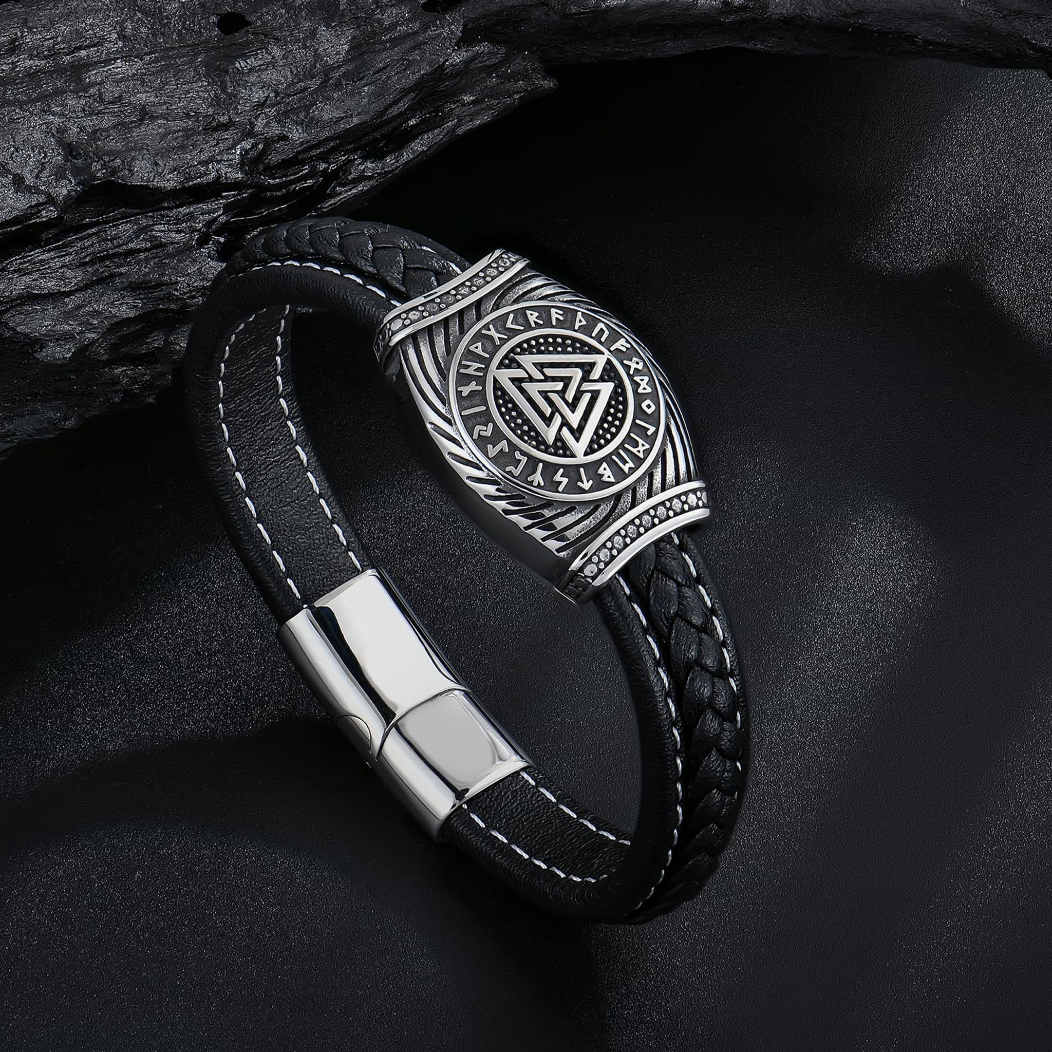Svart läderarmband med flätad struktur, prytt med ett silverfärgat spänne som visar en valknut-symbol med runor runtom