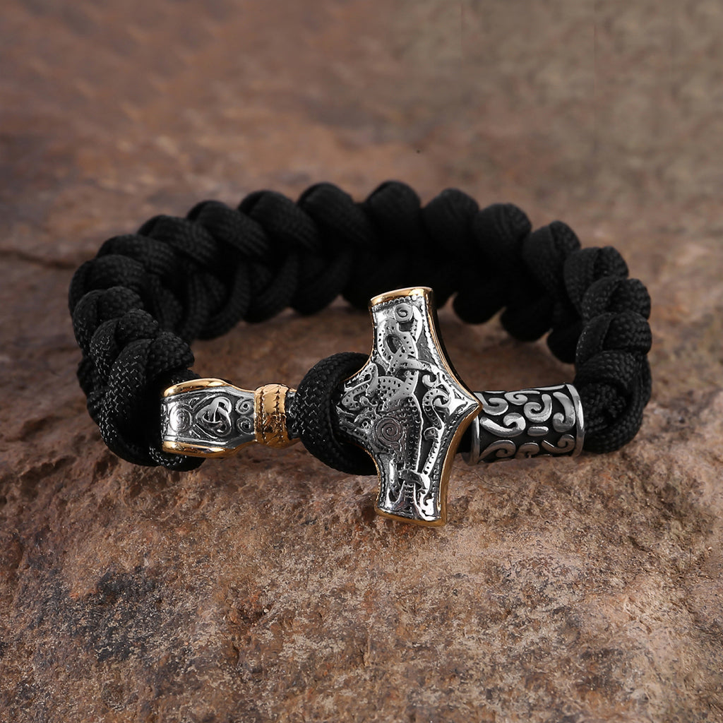Svart paracord-armband med stålsmycke föreställande förgylld torshammare
