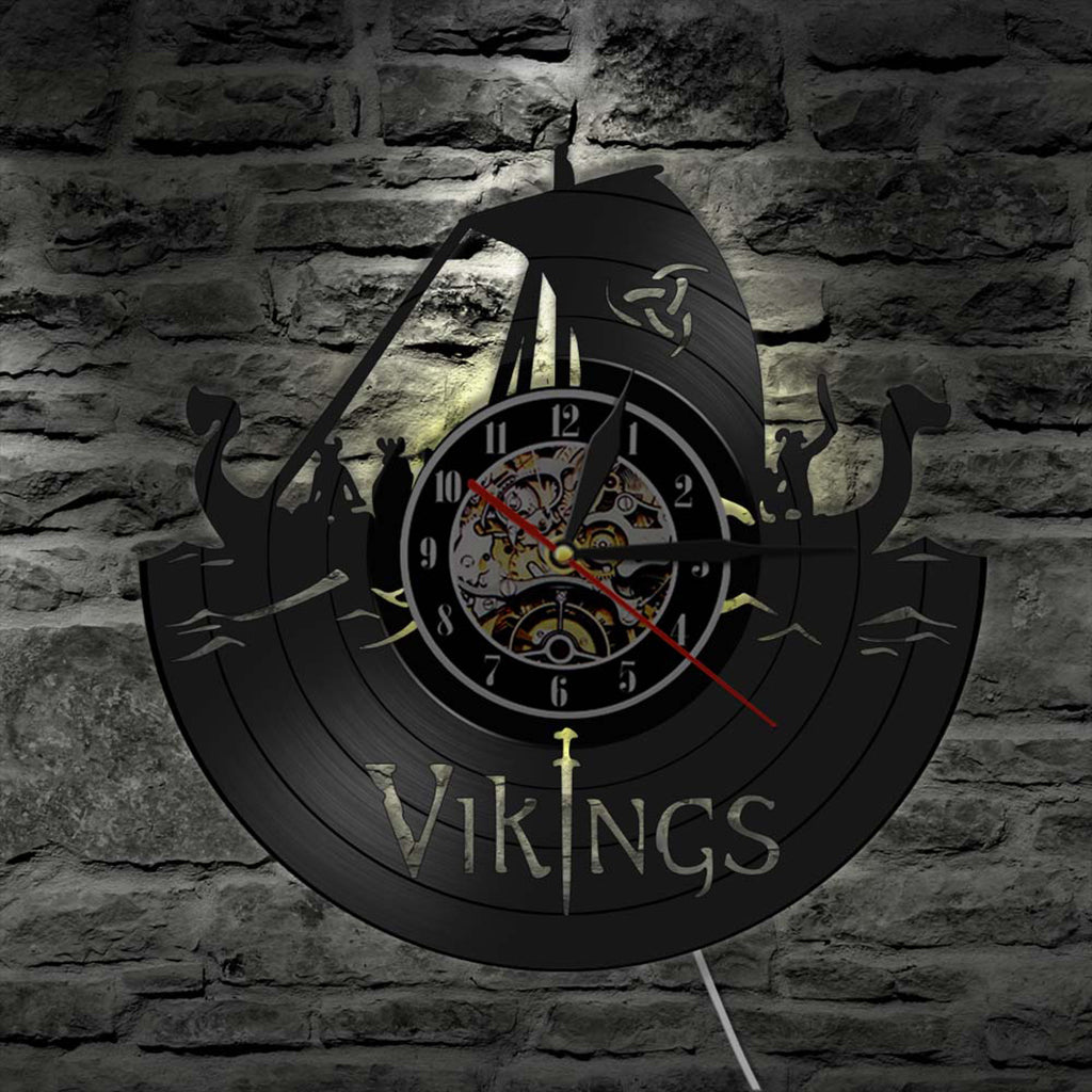 Rund bakgrundsbelyst väggklocka med utskurna vikingasymboler på urtavlan