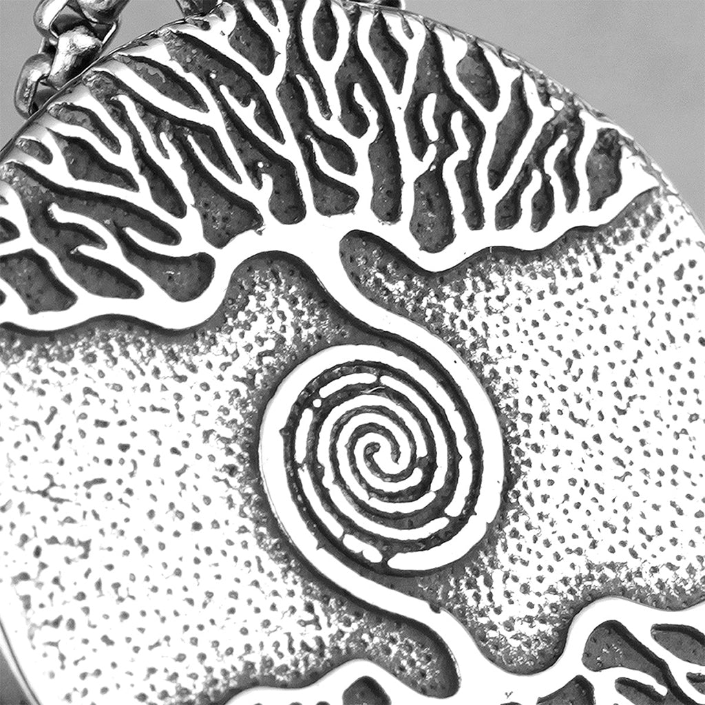 Silverfärgad amulett i stål med gravering föreställande spiralformat träd